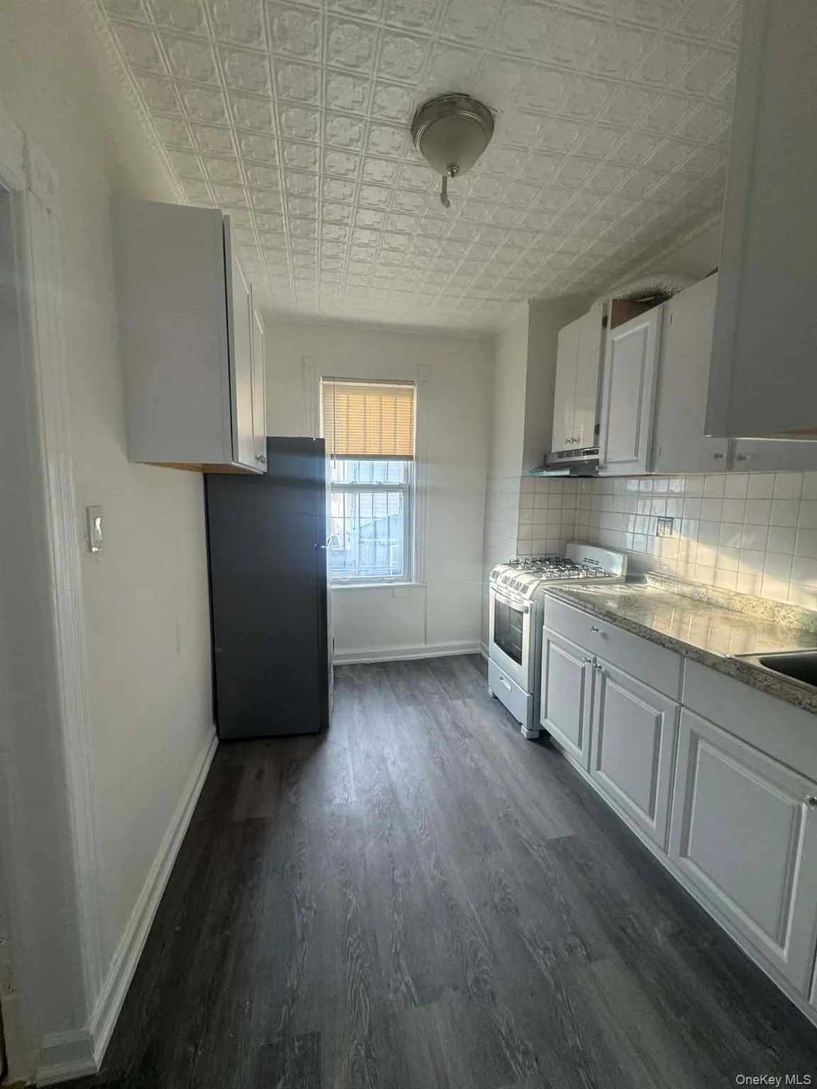 Kitchen with gas range gas stove, freestanding refrigerator, an ornate ceiling, dark wood-style flooring, and white cabinetry Kitchen with gas range gas stove, freestanding refrigerator, an ornate ceiling, dark wood-style flooring, and white cabinetry