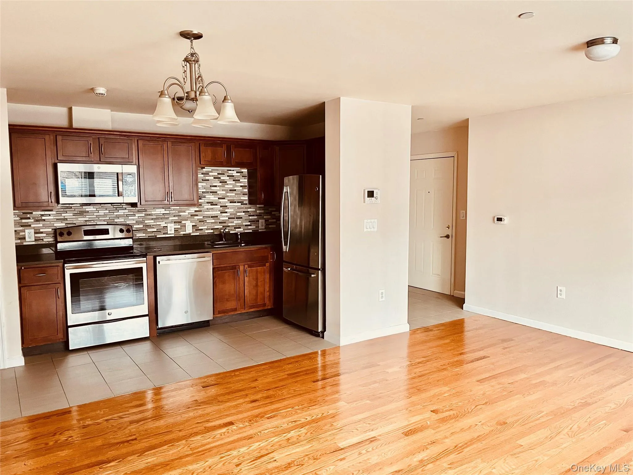 Kitchen featuring appliances with stainless steel finishes, dark countertops, hanging light fixtures, light wood finished floors, and backsplash Kitchen featuring appliances with stainless steel finishes, dark countertops, hanging light fixtures, light wood finished floors, and backsplash