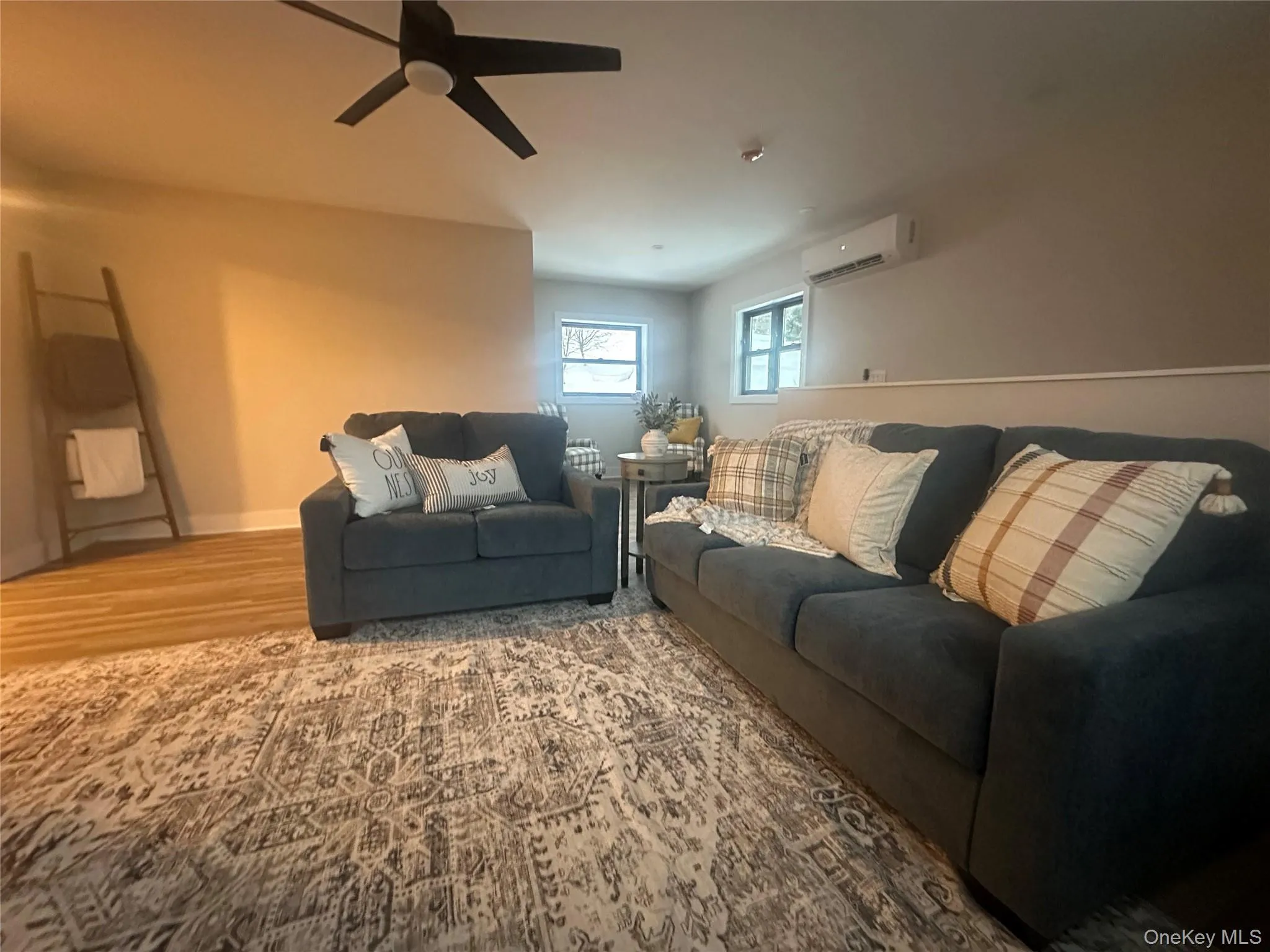 Living area featuring light wood-type flooring, a wall mounted AC, and a ceiling fan Living area featuring light wood-type flooring, a wall mounted AC, and a ceiling fan