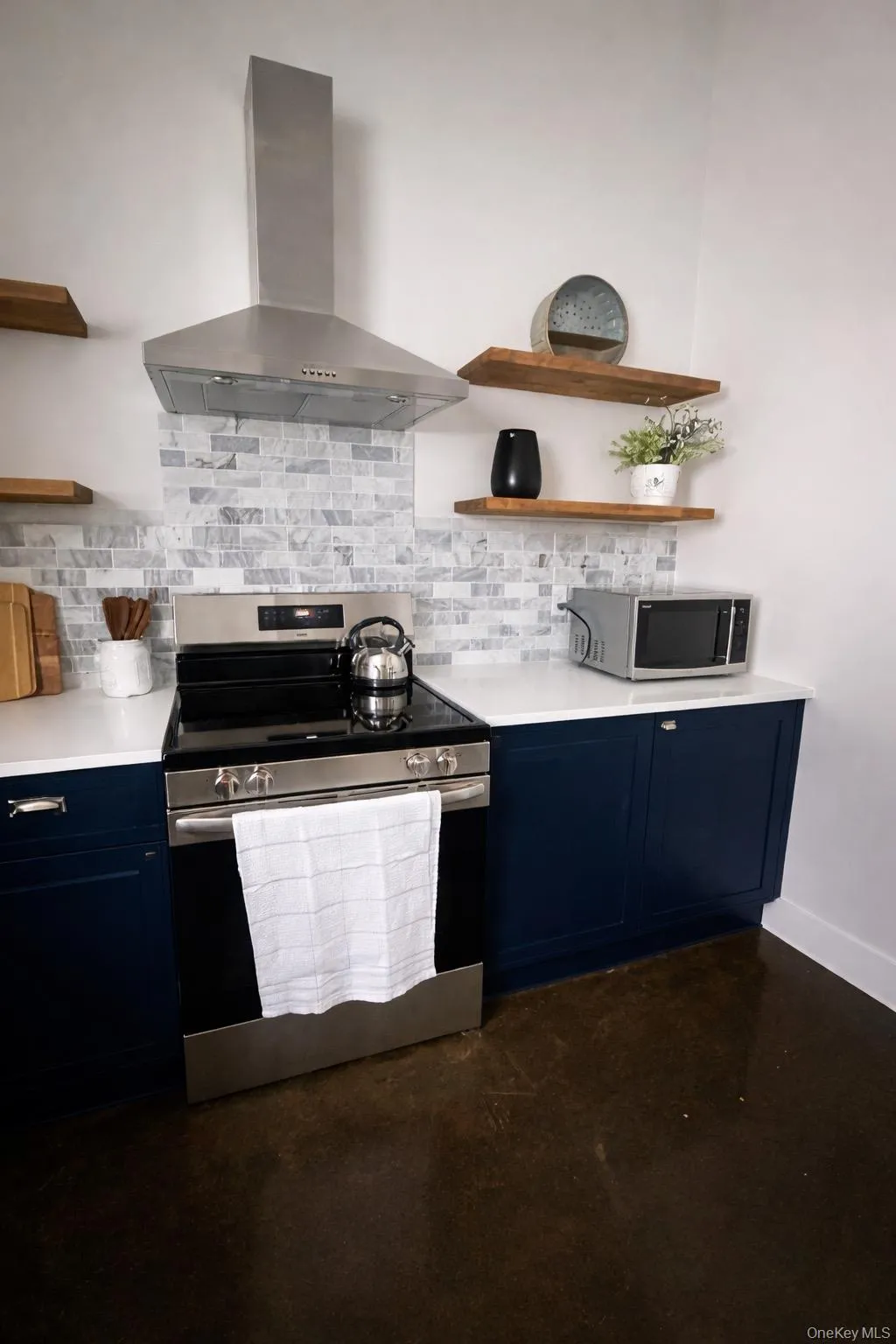 Kitchen featuring open shelves, blue cabinets, appliances with stainless steel finishes, wall chimney range hood, and concrete floors Kitchen featuring open shelves, blue cabinets, appliances with stainless steel finishes, wall chimney range hood, and concrete floors