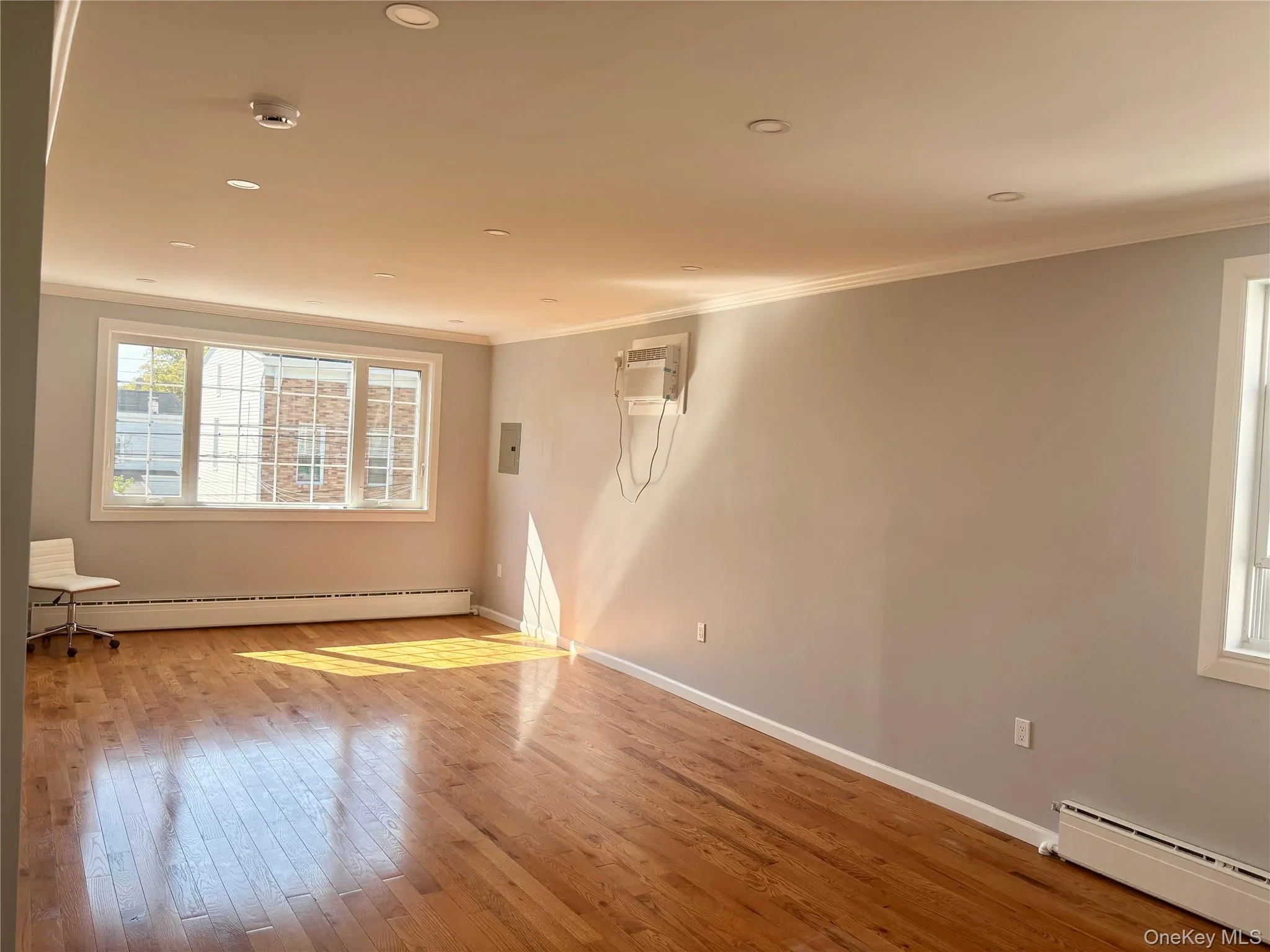 Unfurnished room with a baseboard radiator, crown molding, hardwood / wood-style floors, recessed lighting, and an AC wall unit Unfurnished room with a baseboard radiator, crown molding, hardwood / wood-style floors, recessed lighting, and an AC wall unit