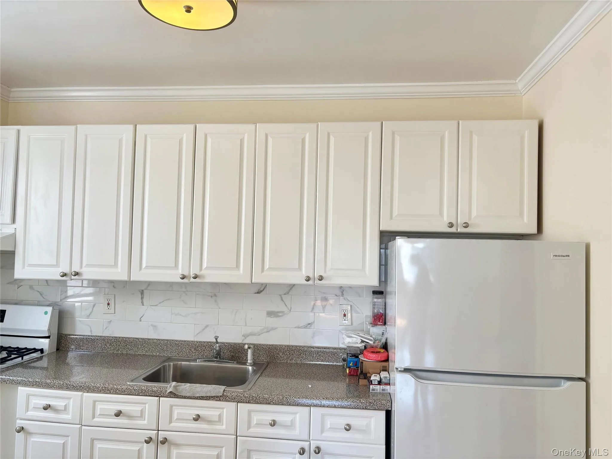 Kitchen with white appliances, white cabinetry, ornamental molding, backsplash, and dark stone countertops Kitchen with white appliances, white cabinetry, ornamental molding, backsplash, and dark stone countertops