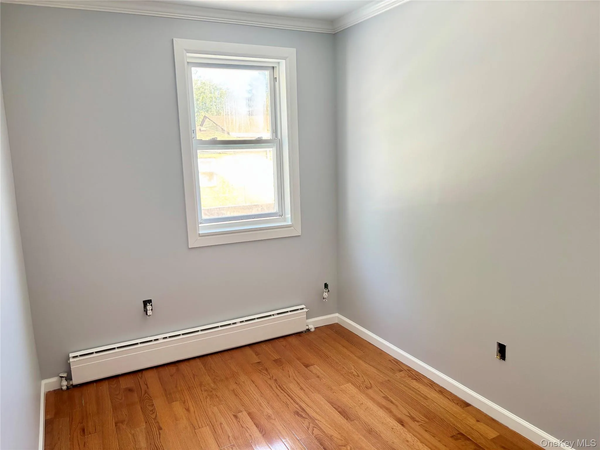 Empty room with a baseboard heating unit, light wood-type flooring, and ornamental molding Empty room with a baseboard heating unit, light wood-type flooring, and ornamental molding