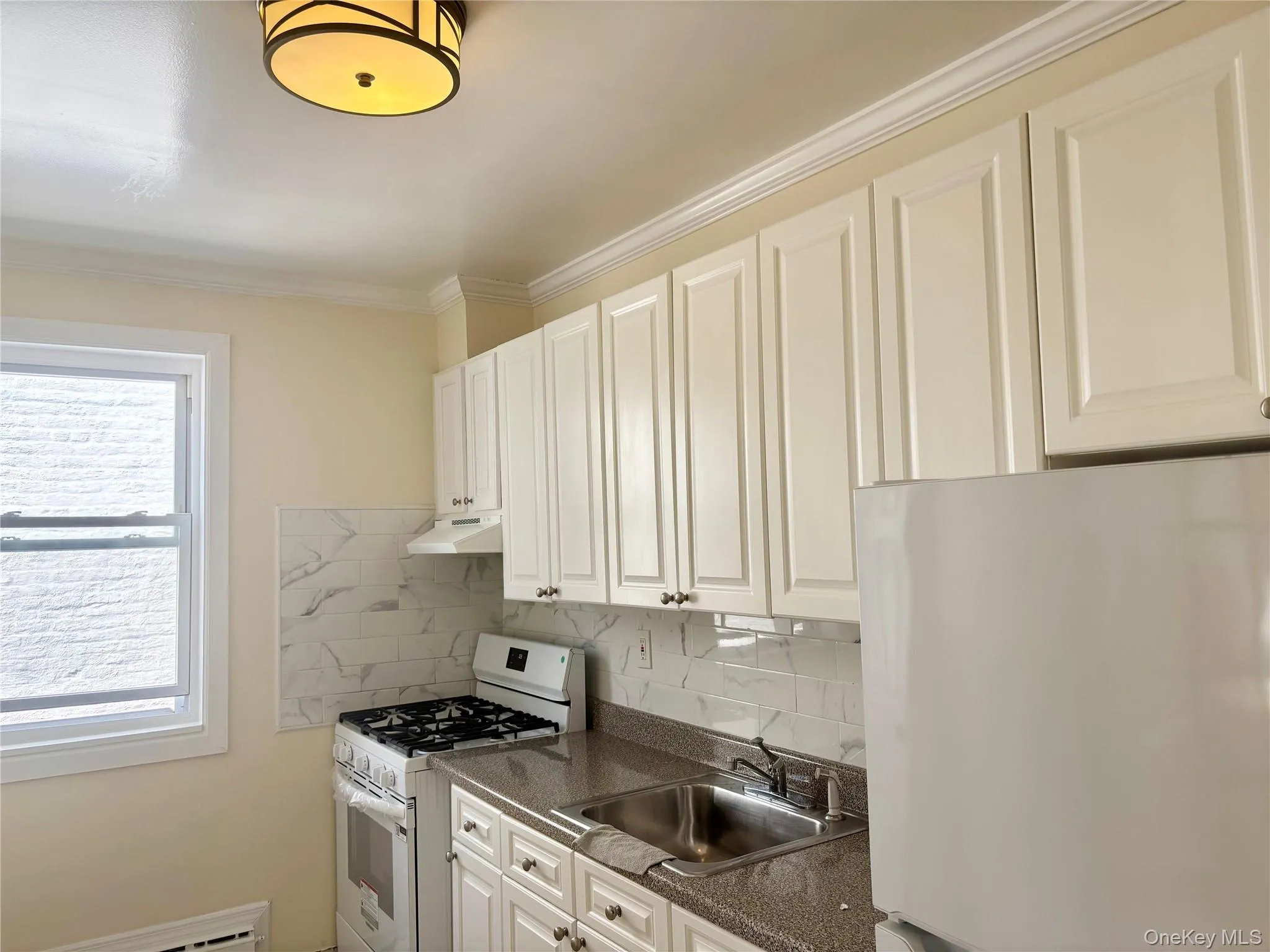 Kitchen featuring white appliances, tasteful backsplash, crown molding, under cabinet range hood, and white cabinets Kitchen featuring white appliances, tasteful backsplash, crown molding, under cabinet range hood, and white cabinets