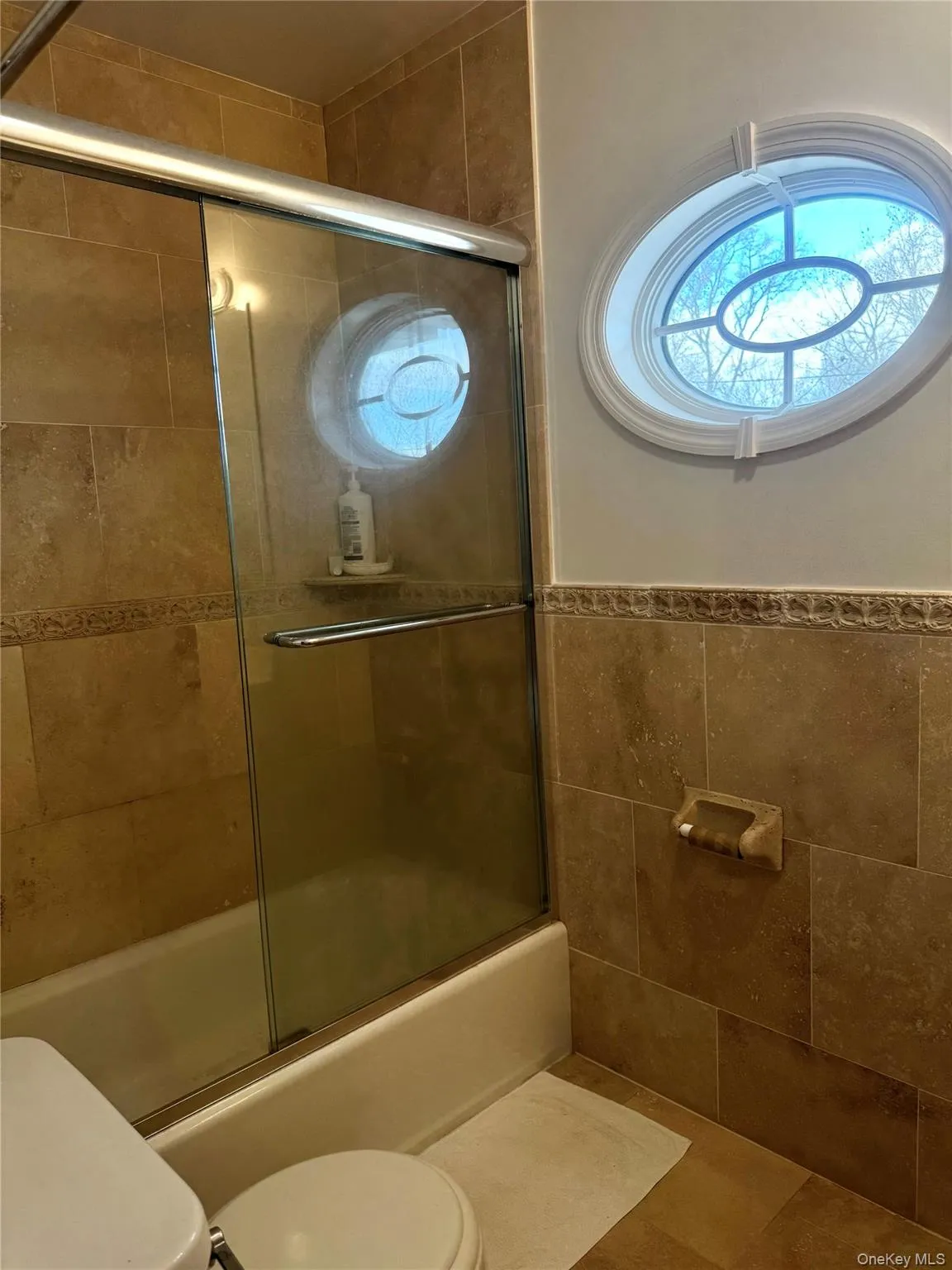 Full bath with bath / shower combo with glass door, wainscoting, and tile walls Full bath with bath / shower combo with glass door, wainscoting, and tile walls