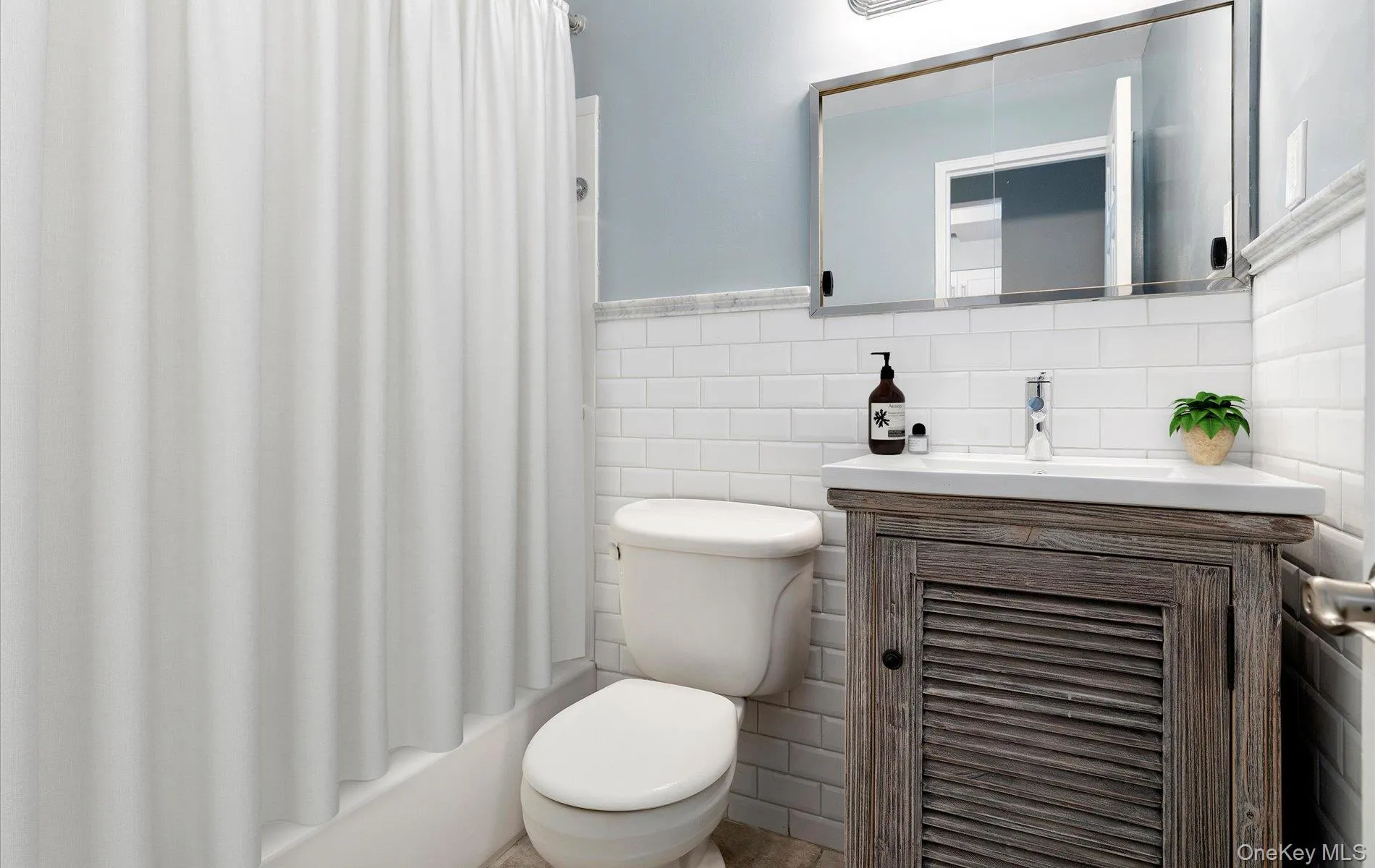 Full bathroom with vanity, tile walls, shower / tub combo with curtain, and wainscoting Full bathroom with vanity, tile walls, shower / tub combo with curtain, and wainscoting