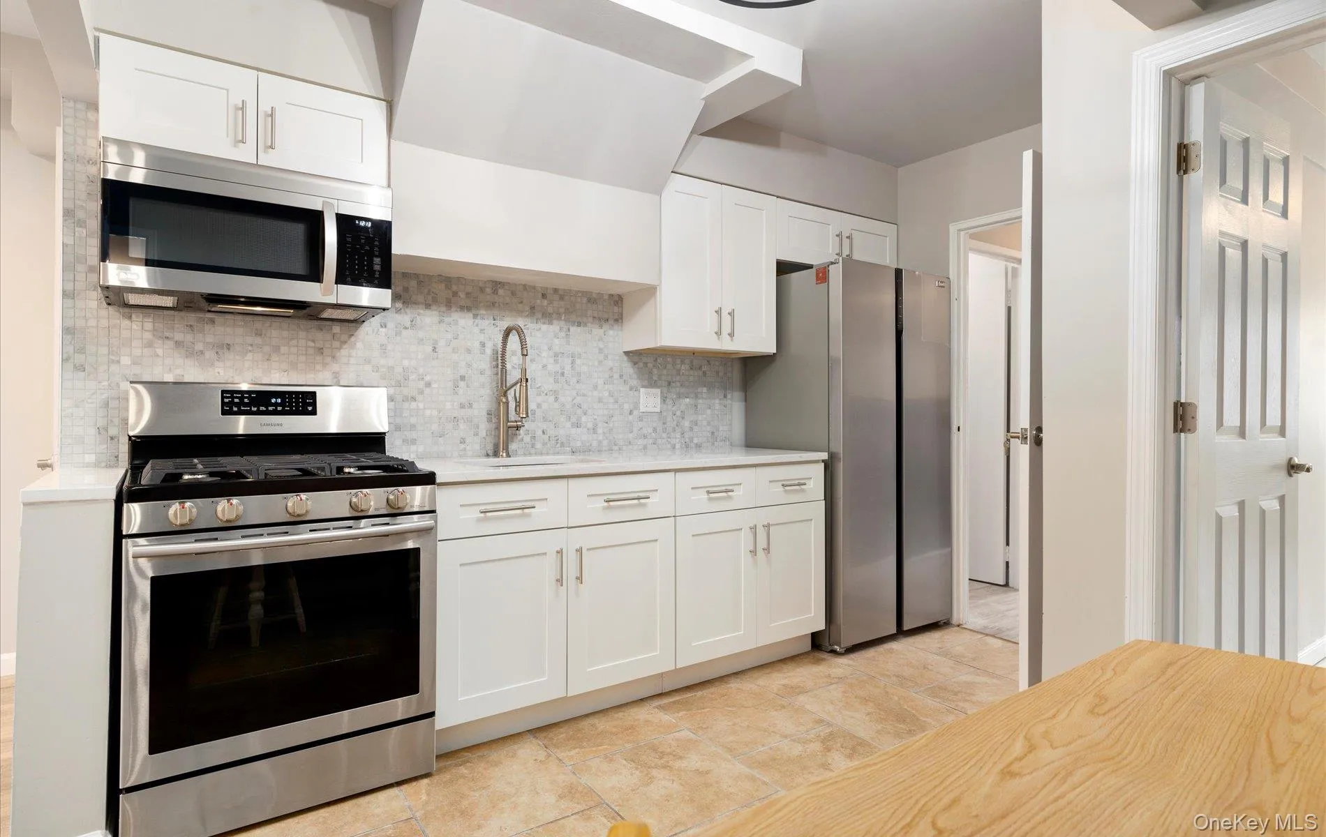 Kitchen with stainless steel appliances, white cabinets, backsplash, and light stone countertops Kitchen with stainless steel appliances, white cabinets, backsplash, and light stone countertops