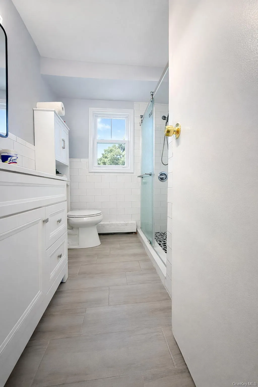 Full bathroom featuring vanity, a stall shower, tile walls, a baseboard radiator, and wainscoting Full bathroom featuring vanity, a stall shower, tile walls, a baseboard radiator, and wainscoting