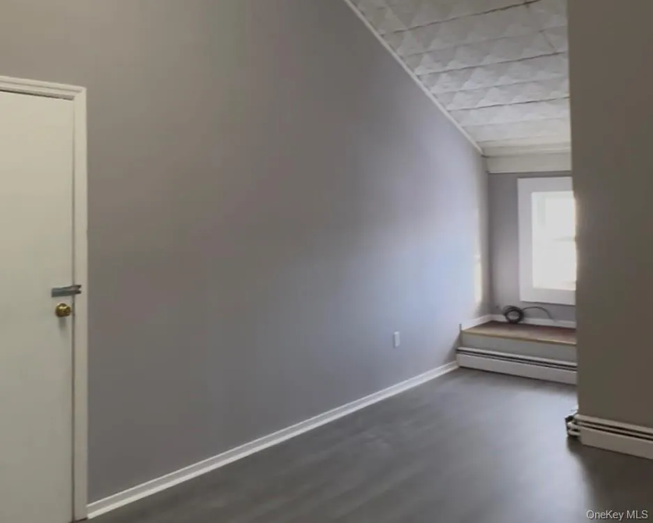 Unfurnished room with a baseboard radiator and dark wood finished floors Unfurnished room with a baseboard radiator and dark wood finished floors