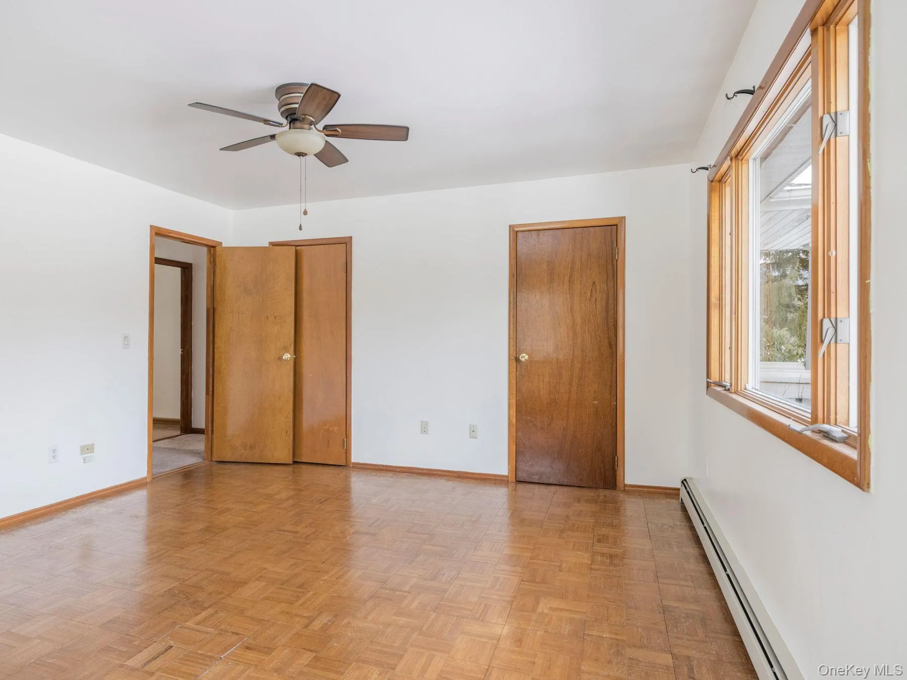 Unfurnished bedroom featuring two closets, baseboard heating, and a ceiling fan Unfurnished bedroom featuring two closets, baseboard heating, and a ceiling fan