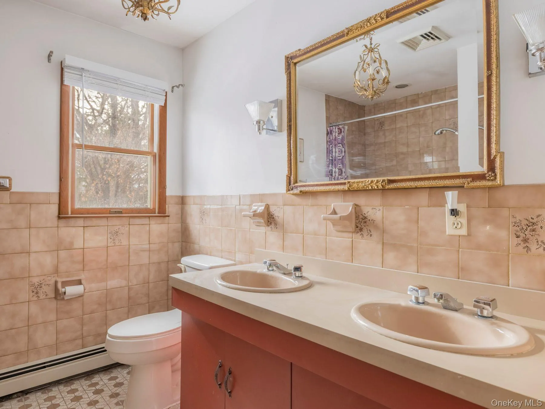 Bathroom featuring a baseboard heating unit, double vanity, tiled shower, a chandelier, and wainscoting Bathroom featuring a baseboard heating unit, double vanity, tiled shower, a chandelier, and wainscoting
