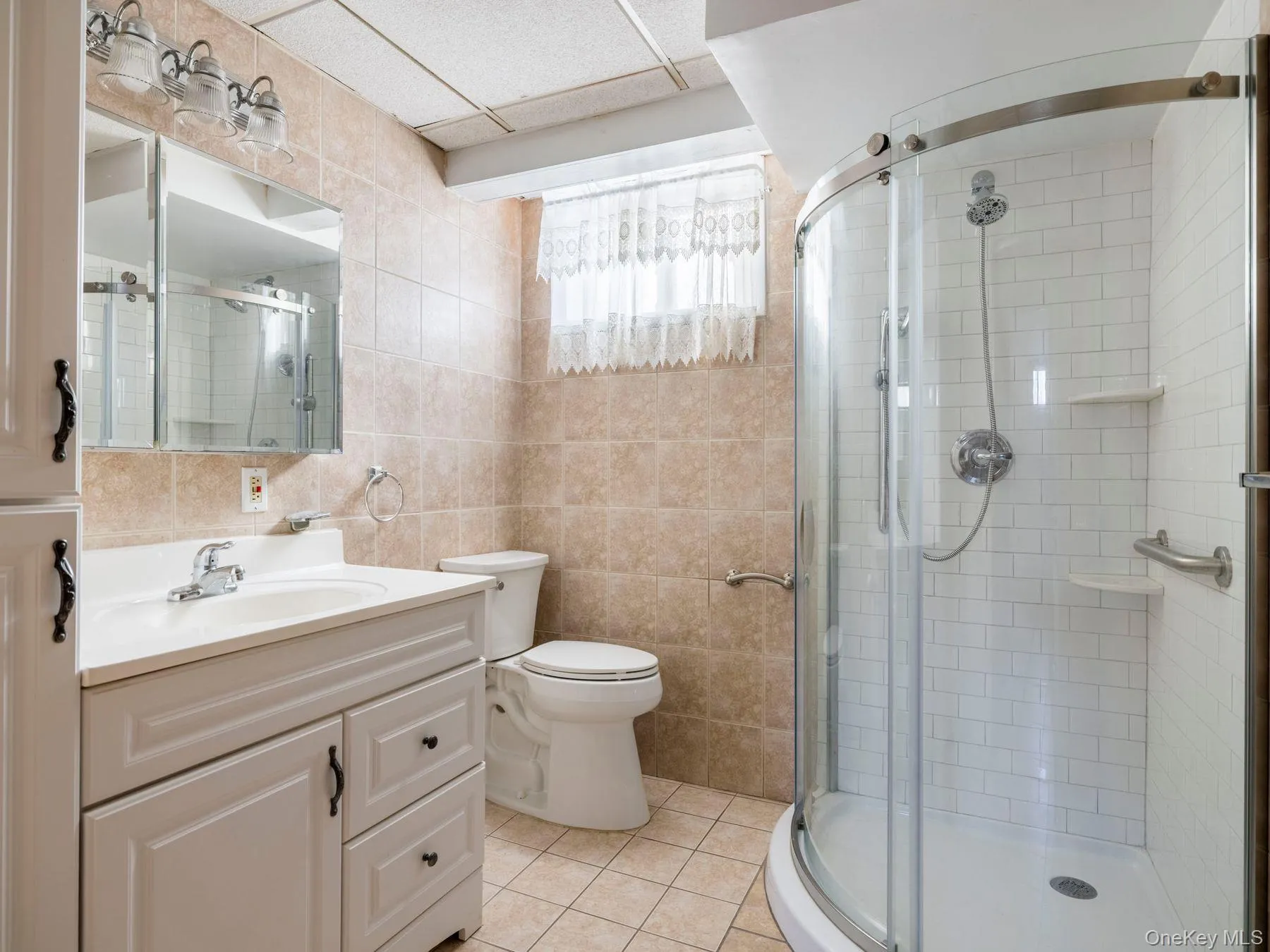 Full bath featuring tile walls, vanity, a shower stall, and light tile patterned flooring Full bath featuring tile walls, vanity, a shower stall, and light tile patterned flooring