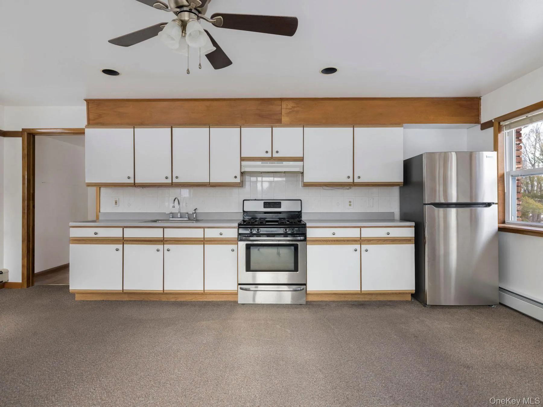 Kitchen with white cabinets, appliances with stainless steel finishes, light countertops, ceiling fan, and under cabinet range hood Kitchen with white cabinets, appliances with stainless steel finishes, light countertops, ceiling fan, and under cabinet range hood