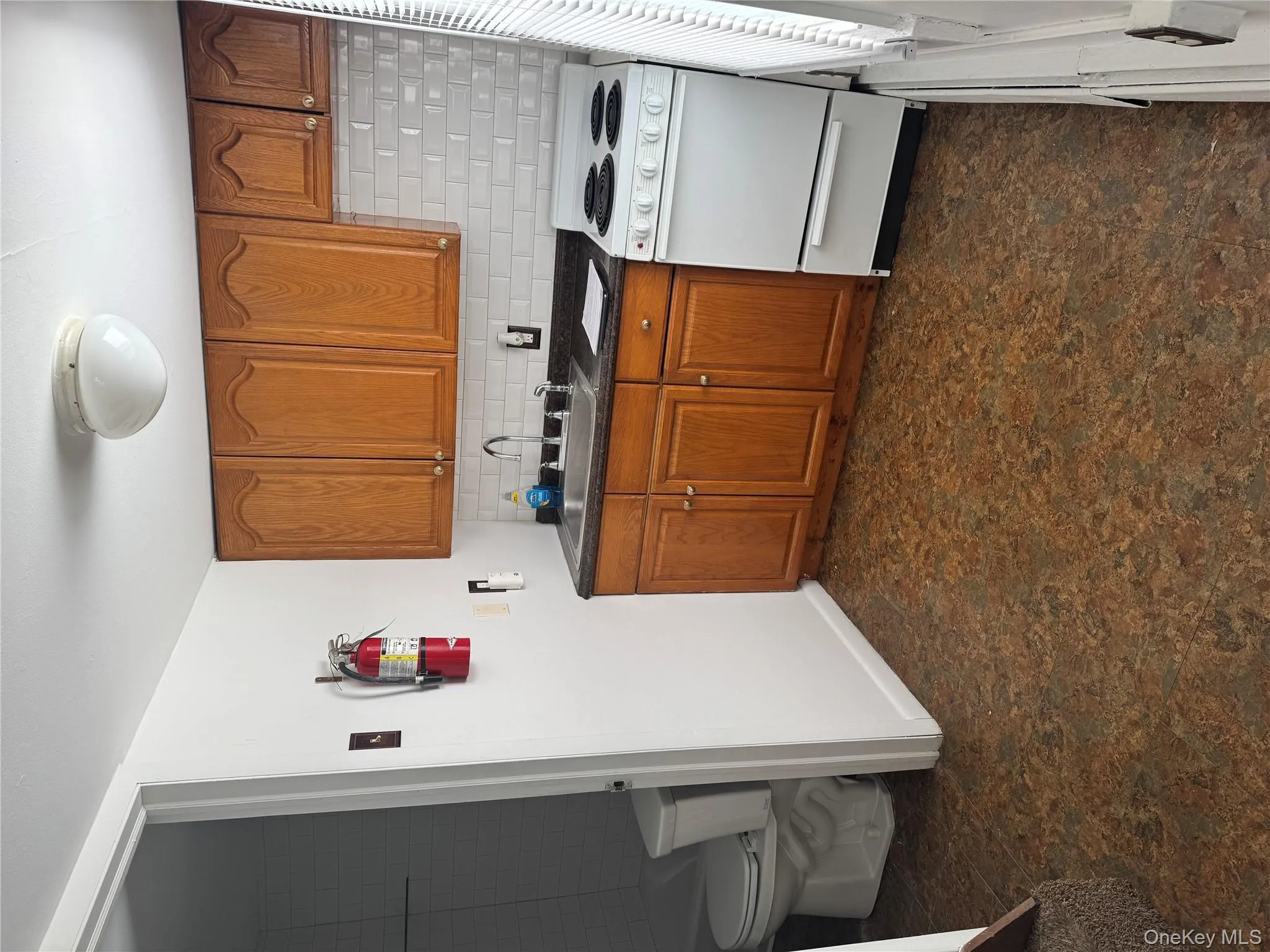 Kitchen with range, brown cabinetry, dark countertops, decorative backsplash, and dark floors Kitchen with range, brown cabinetry, dark countertops, decorative backsplash, and dark floors