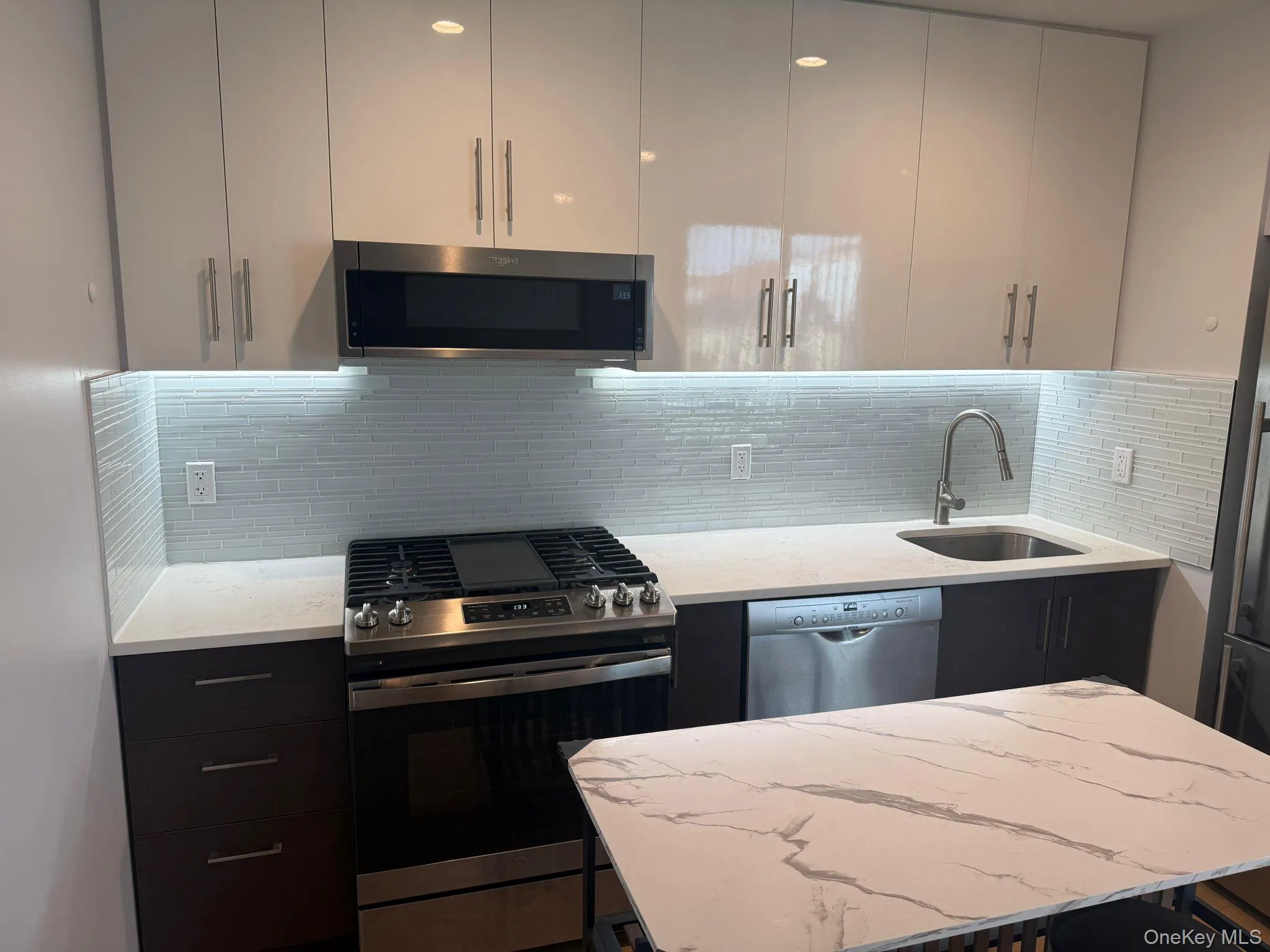 Kitchen with stainless steel appliances, light stone countertops, backsplash, dark cabinets, and a breakfast bar Kitchen with stainless steel appliances, light stone countertops, backsplash, dark cabinets, and a breakfast bar