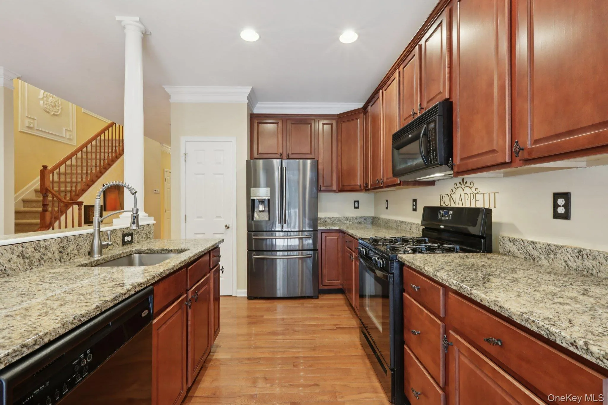 Kitchen with black appliances, light stone countertops, light hardwood flooring, ornamental molding, and recessed lighting Kitchen with black appliances, light stone countertops, light hardwood flooring, ornamental molding, and recessed lighting