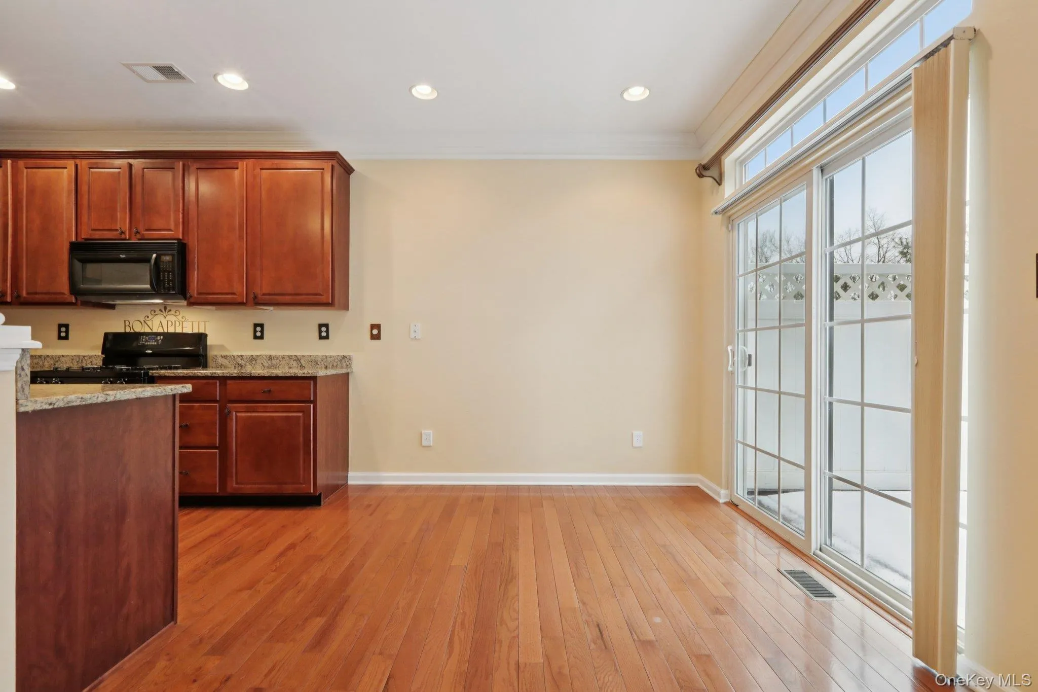 Kitchen with light stone countertops, ornamental molding, black appliances, light wood flooring, and recessed lighting Kitchen with light stone countertops, ornamental molding, black appliances, light wood flooring, and recessed lighting