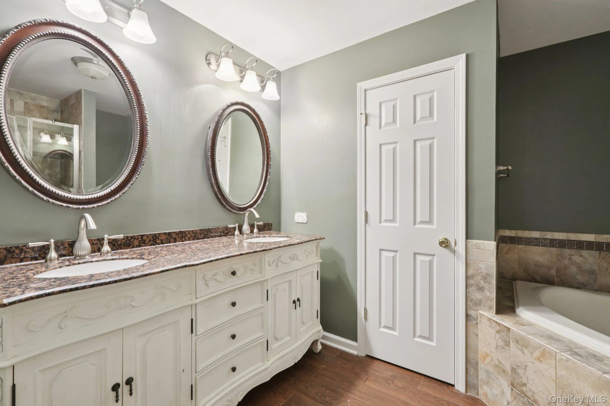 Full bath featuring double vanity, tiled tub, dark wood-style floors, and a shower with shower door Full bath featuring double vanity, tiled tub, dark wood-style floors, and a shower with shower door