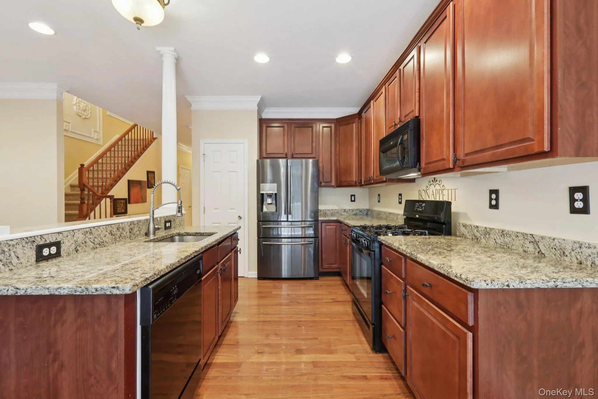 Kitchen featuring black appliances, light stone counters, ornamental molding, light hardwood flooring, and recessed lighting Kitchen featuring black appliances, light stone counters, ornamental molding, light hardwood flooring, and recessed lighting