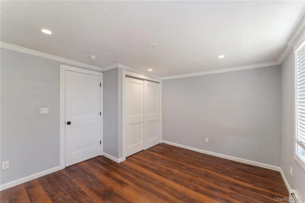 Unfurnished bedroom with a closet, dark wood finished floors, recessed lighting, ornamental molding, and a baseboard heating unit Unfurnished bedroom with a closet, dark wood finished floors, recessed lighting, ornamental molding, and a baseboard heating unit