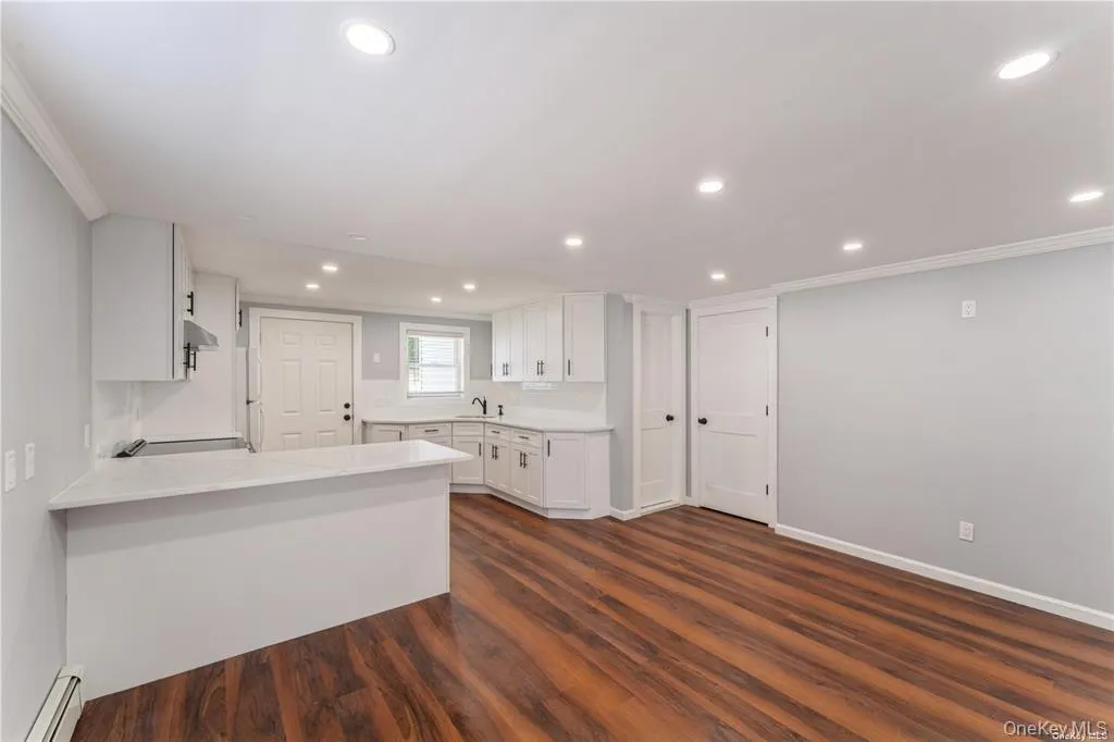 Kitchen with white cabinetry, a peninsula, dark wood finished floors, a baseboard radiator, and ornamental molding Kitchen with white cabinetry, a peninsula, dark wood finished floors, a baseboard radiator, and ornamental molding