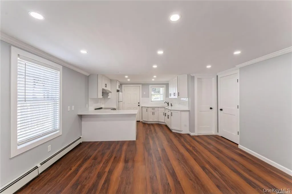 Kitchen with baseboard heating, light countertops, white cabinetry, a peninsula, and crown molding Kitchen with baseboard heating, light countertops, white cabinetry, a peninsula, and crown molding