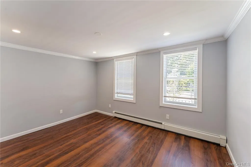 Empty room with a baseboard radiator, dark wood finished floors, crown molding, and recessed lighting Empty room with a baseboard radiator, dark wood finished floors, crown molding, and recessed lighting