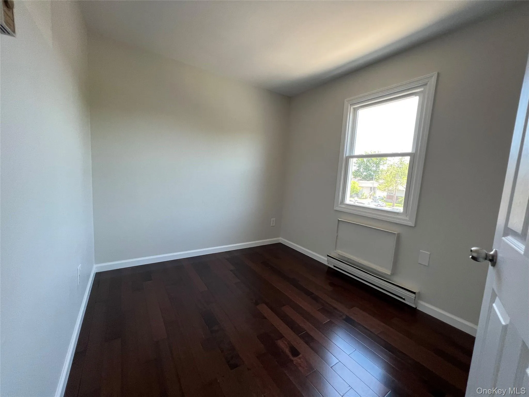 Spare room with a baseboard heating unit and dark wood-type flooring Spare room with a baseboard heating unit and dark wood-type flooring