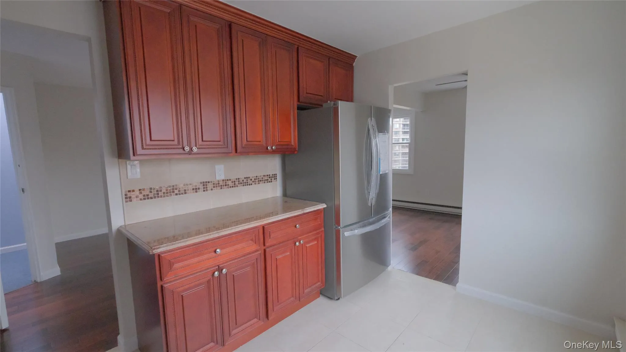 Kitchen featuring light stone counters, backsplash, a baseboard heating unit, freestanding refrigerator, and reddish brown cabinets Kitchen featuring light stone counters, backsplash, a baseboard heating unit, freestanding refrigerator, and reddish brown cabinets