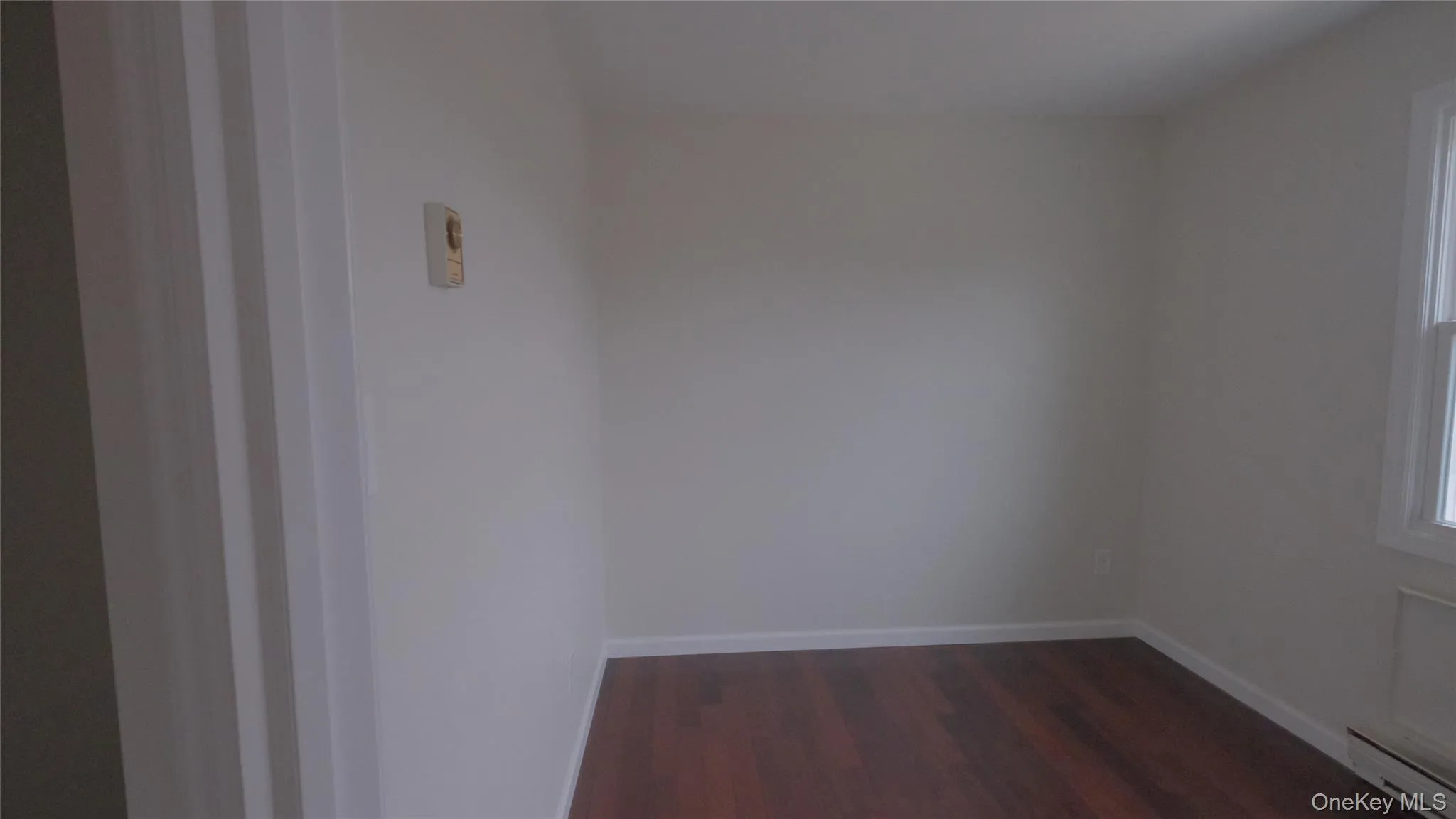 Unfurnished room featuring dark wood finished floors and baseboard heating Unfurnished room featuring dark wood finished floors and baseboard heating