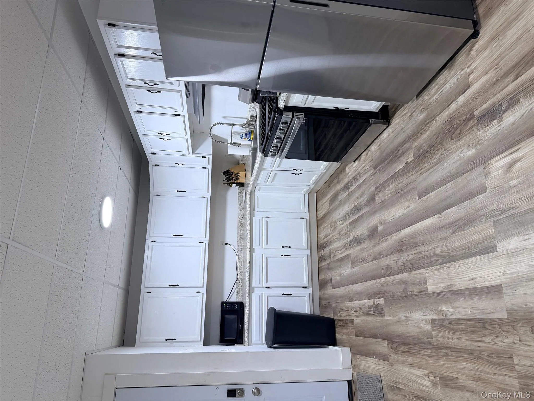 Kitchen featuring refrigerator, white cabinetry, stove, a paneled ceiling, and light wood finished floors Kitchen featuring refrigerator, white cabinetry, stove, a paneled ceiling, and light wood finished floors