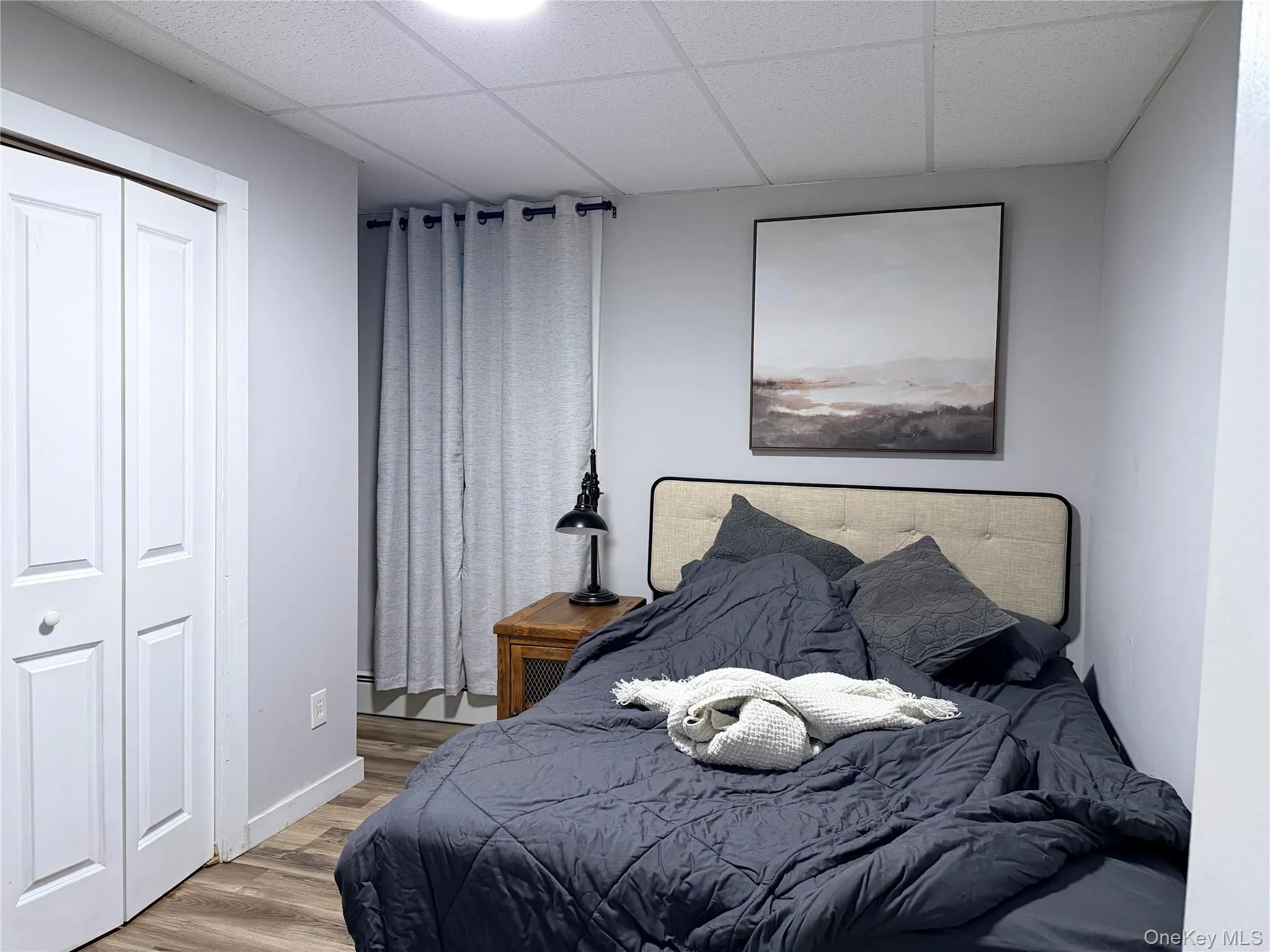 Bedroom featuring a drop ceiling, wood finished floors, and a closet Bedroom featuring a drop ceiling, wood finished floors, and a closet