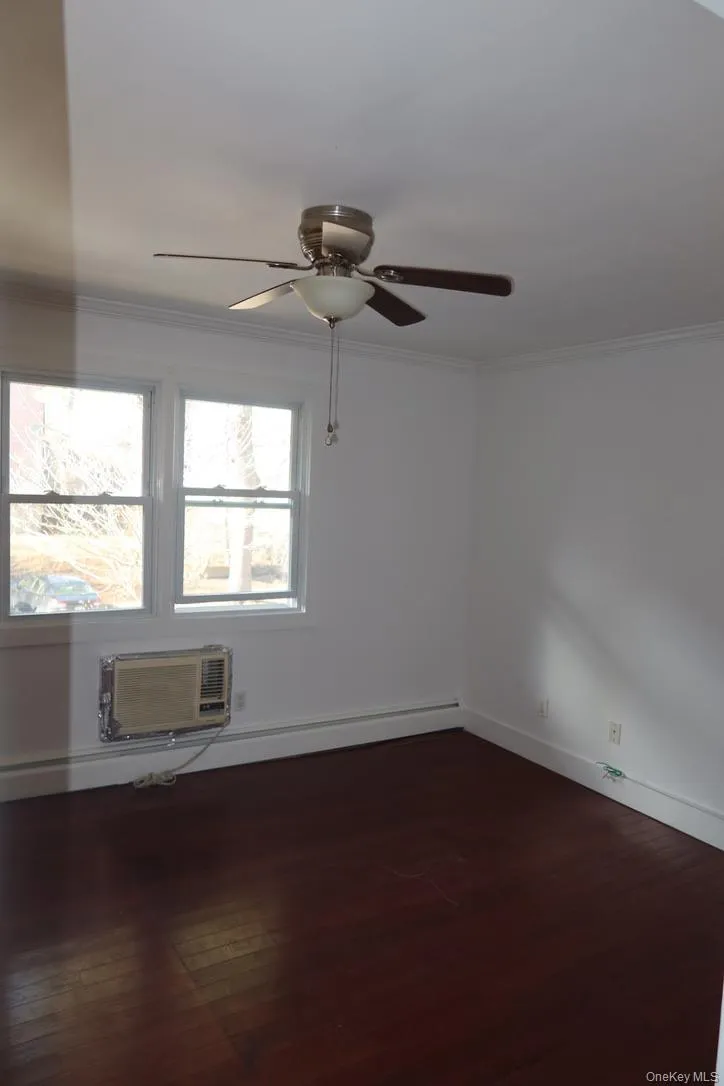 Spare room featuring crown molding, a baseboard heating unit, dark wood finished floors, ceiling fan, and a wall mounted AC Spare room featuring crown molding, a baseboard heating unit, dark wood finished floors, ceiling fan, and a wall mounted AC