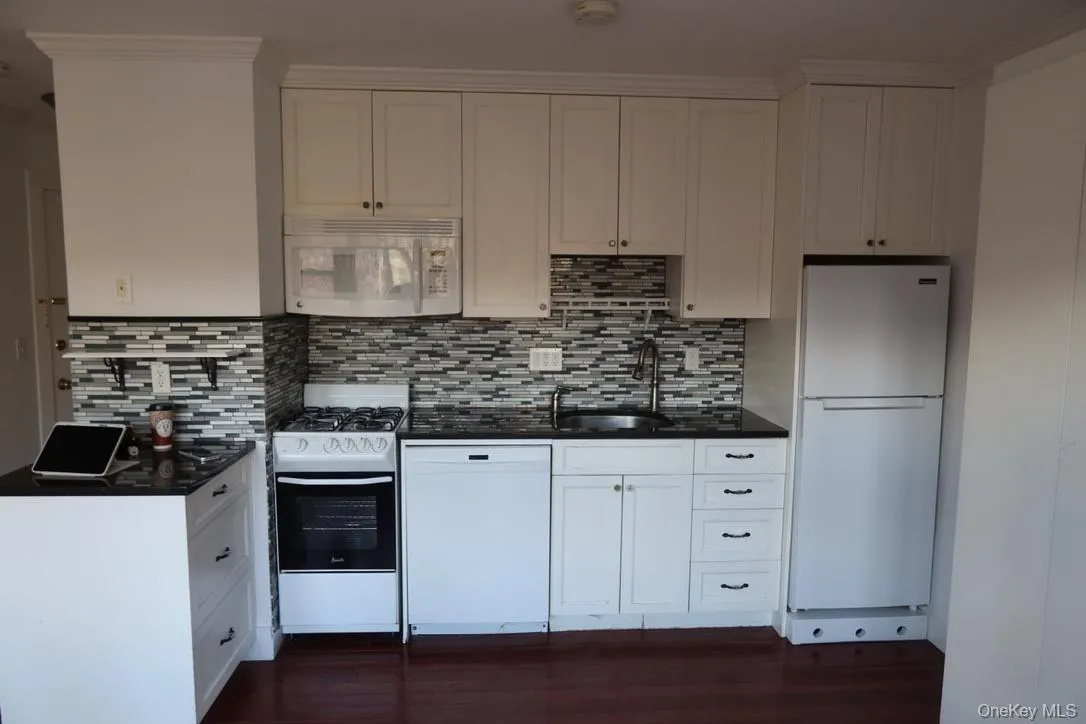 Kitchen with white appliances, white cabinetry, dark wood-style flooring, and decorative backsplash Kitchen with white appliances, white cabinetry, dark wood-style flooring, and decorative backsplash