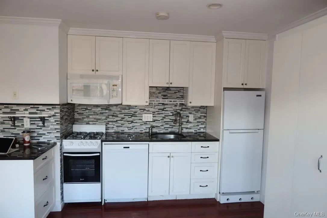 Kitchen featuring white appliances, white cabinets, and dark stone countertops Kitchen featuring white appliances, white cabinets, and dark stone countertops
