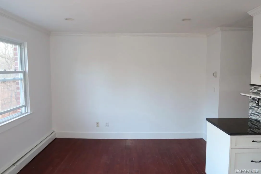 Unfurnished dining area with a baseboard radiator, crown molding, and dark wood-style floors Unfurnished dining area with a baseboard radiator, crown molding, and dark wood-style floors