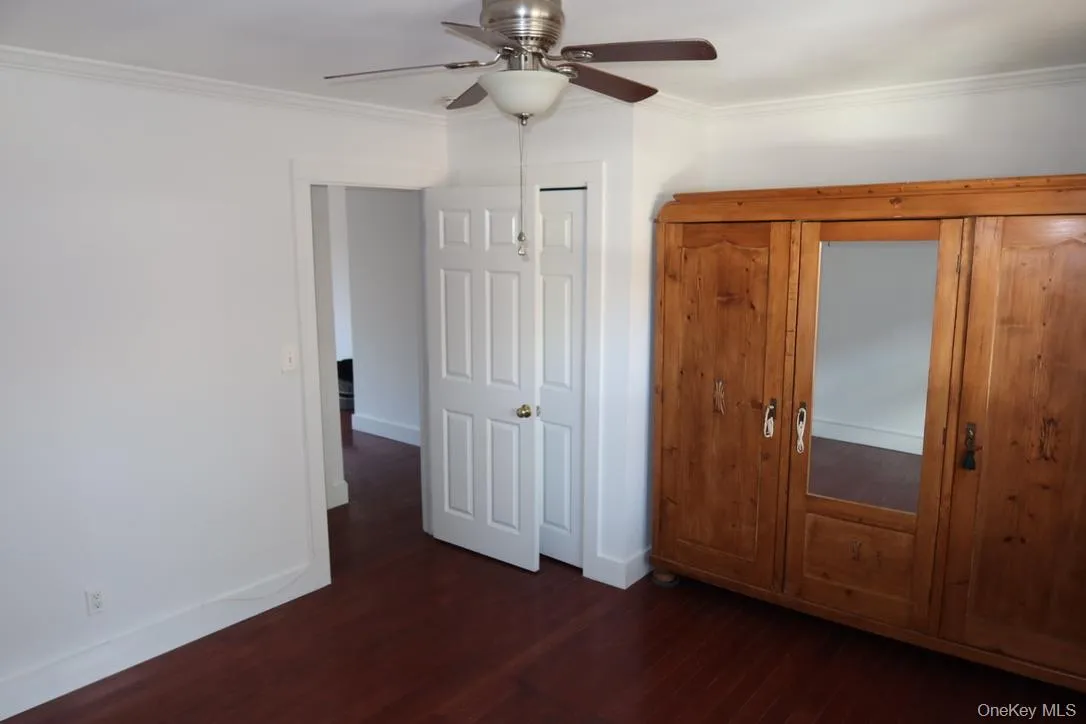 Unfurnished bedroom with crown molding, dark wood-type flooring, and a ceiling fan Unfurnished bedroom with crown molding, dark wood-type flooring, and a ceiling fan