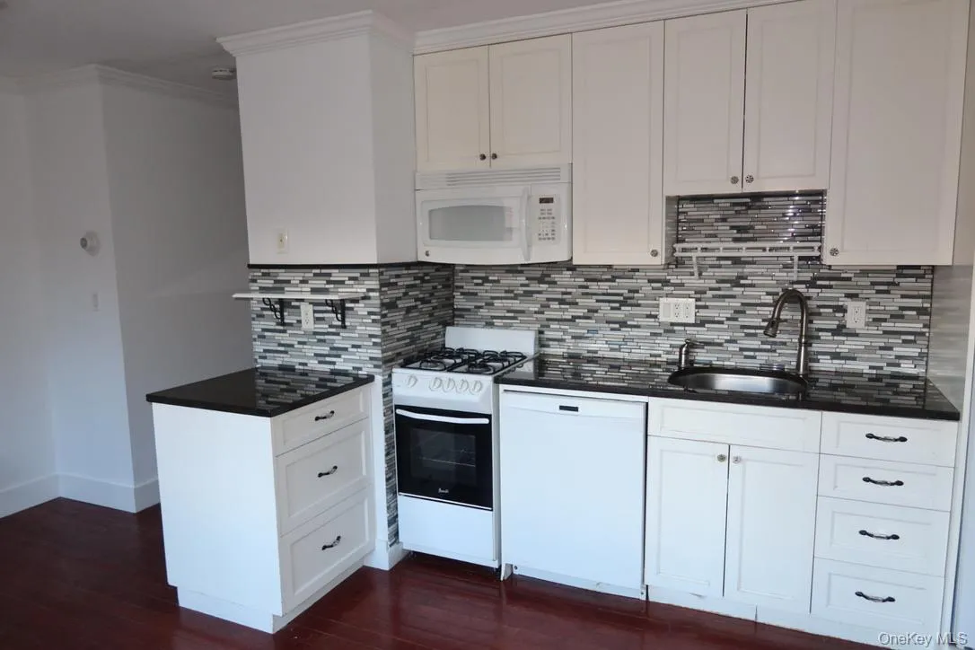 Kitchen with white appliances, white cabinets, dark wood finished floors, backsplash, and ornamental molding Kitchen with white appliances, white cabinets, dark wood finished floors, backsplash, and ornamental molding