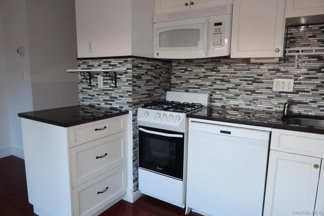 Kitchen featuring white appliances, white cabinets, backsplash, dark stone countertops, and dark wood finished floors Kitchen featuring white appliances, white cabinets, backsplash, dark stone countertops, and dark wood finished floors