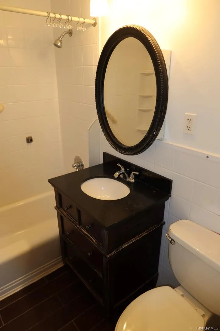 Bathroom featuring vanity, bathtub / shower combination, tile walls, and a wainscoted wall Bathroom featuring vanity, bathtub / shower combination, tile walls, and a wainscoted wall