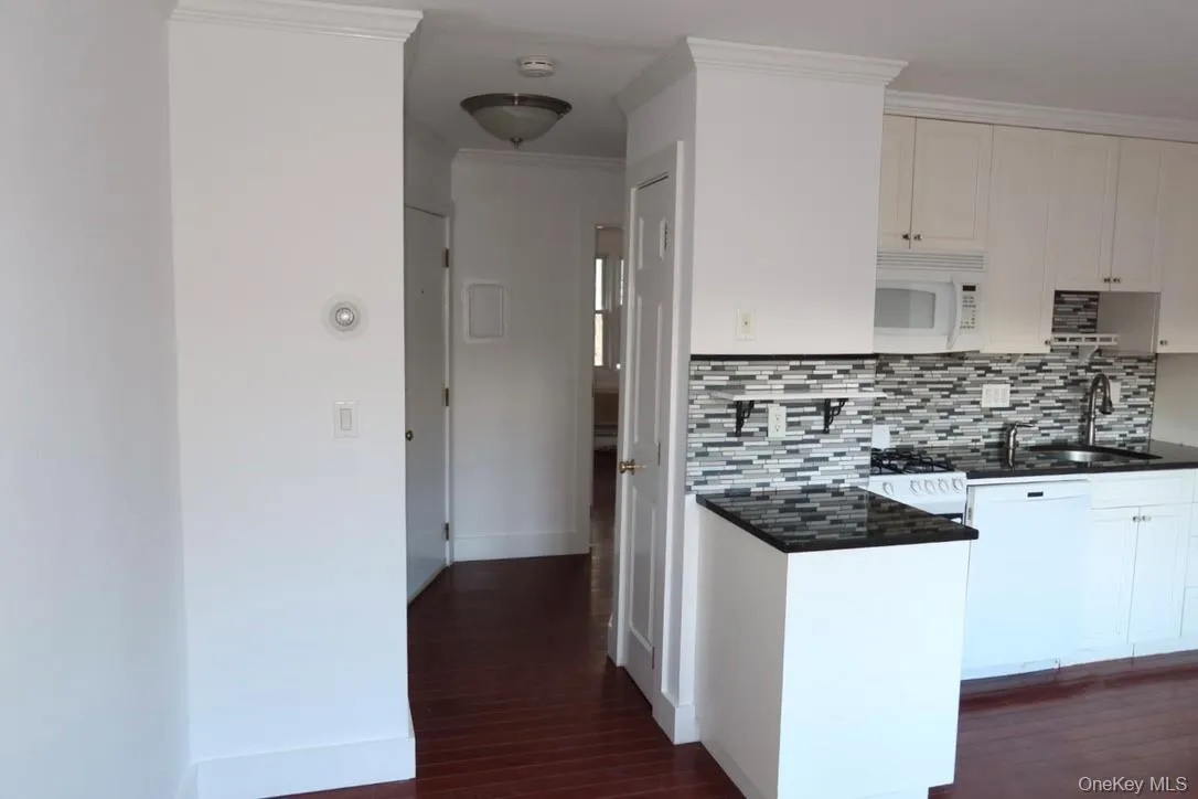 Kitchen with white microwave, white cabinetry, tasteful backsplash, crown molding, and dark wood-style floors Kitchen with white microwave, white cabinetry, tasteful backsplash, crown molding, and dark wood-style floors