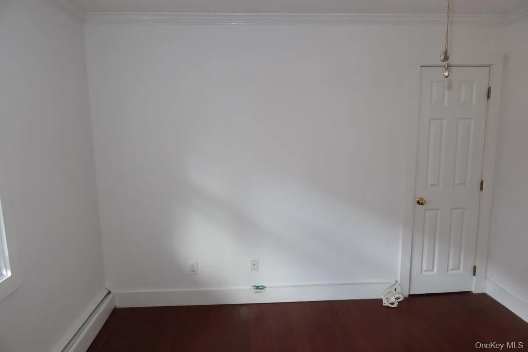 Spare room with a baseboard heating unit, dark wood-style floors, and ornamental molding Spare room with a baseboard heating unit, dark wood-style floors, and ornamental molding