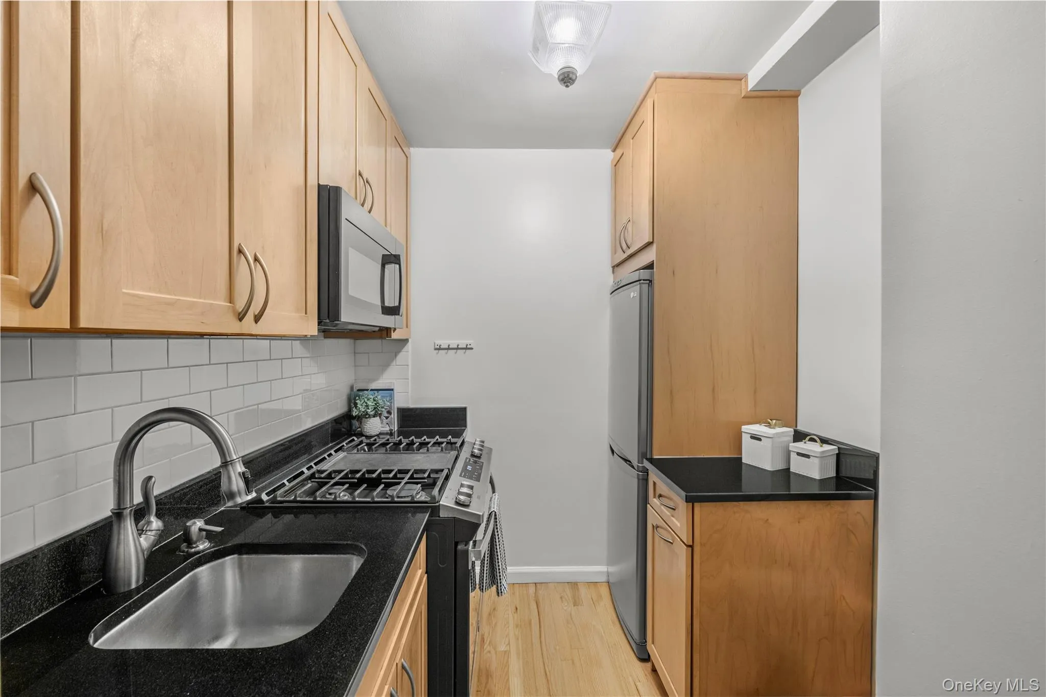 Kitchen with appliances with stainless steel finishes, backsplash, light brown cabinets, light wood-style floors, and dark stone countertops Kitchen with appliances with stainless steel finishes, backsplash, light brown cabinets, light wood-style floors, and dark stone countertops