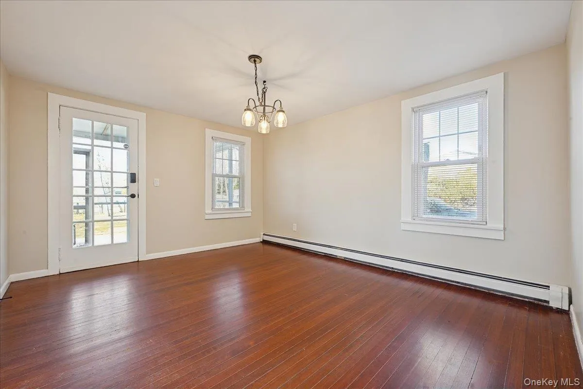 Unfurnished room featuring a baseboard radiator, dark wood-style floors, and a chandelier Unfurnished room featuring a baseboard radiator, dark wood-style floors, and a chandelier