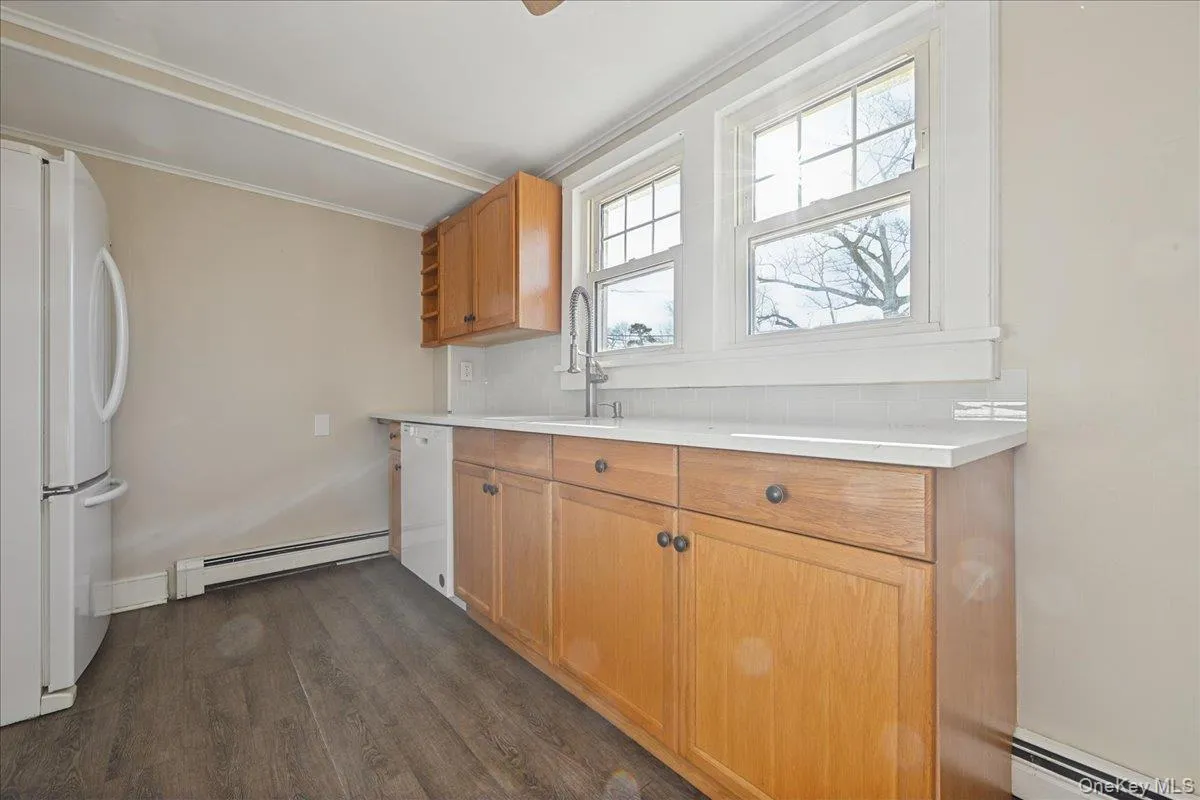 Kitchen featuring light countertops, white appliances, dark wood finished floors, baseboard heating, and crown molding Kitchen featuring light countertops, white appliances, dark wood finished floors, baseboard heating, and crown molding