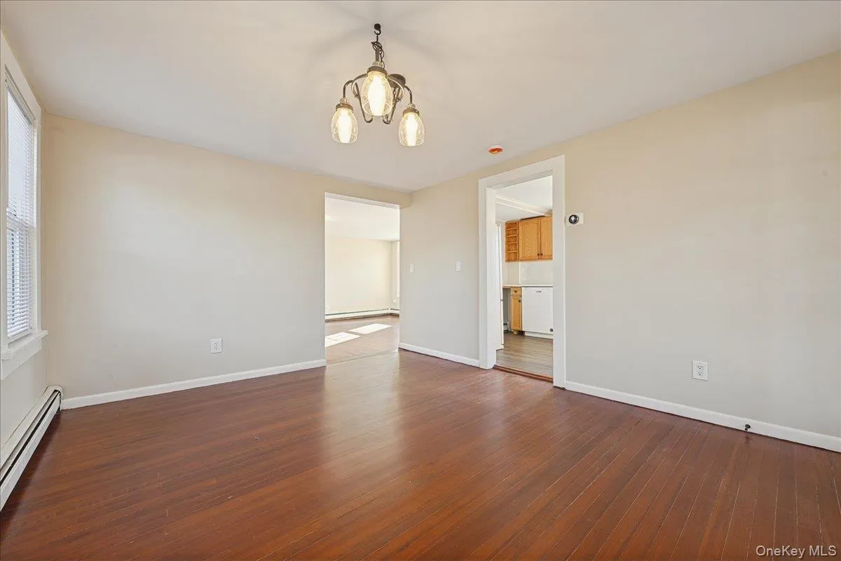 Unfurnished room featuring a chandelier, a baseboard heating unit, and dark wood-type flooring Unfurnished room featuring a chandelier, a baseboard heating unit, and dark wood-type flooring