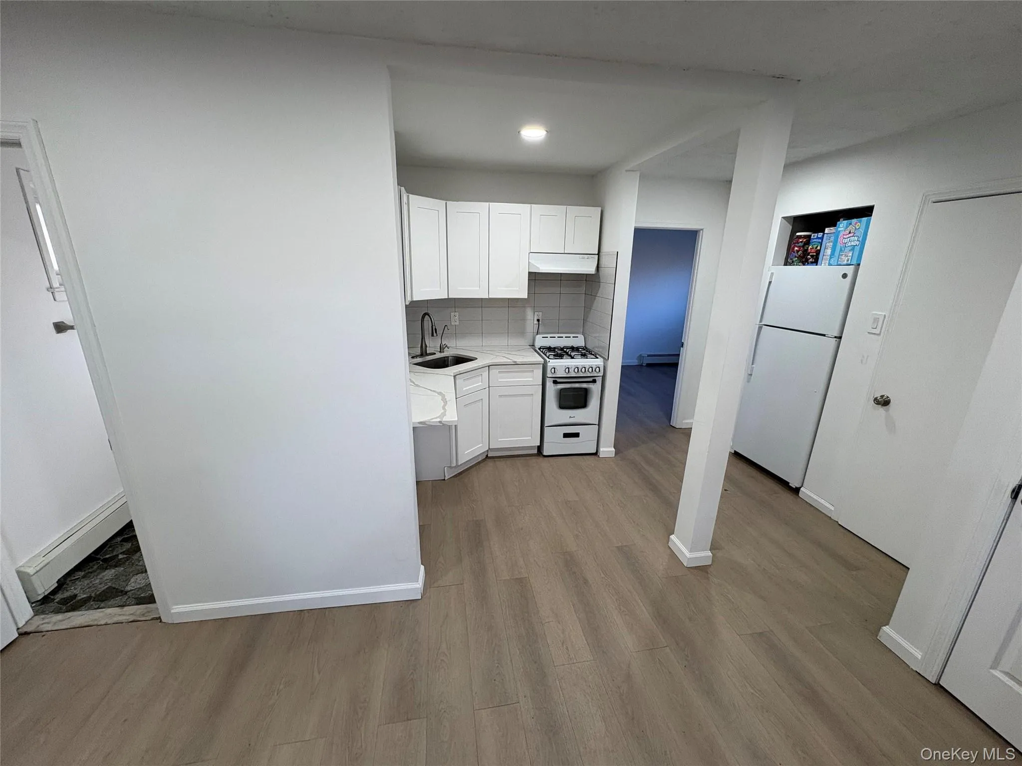 Kitchen featuring light countertops, white cabinets, white appliances, backsplash, and light wood-style floors Kitchen featuring light countertops, white cabinets, white appliances, backsplash, and light wood-style floors