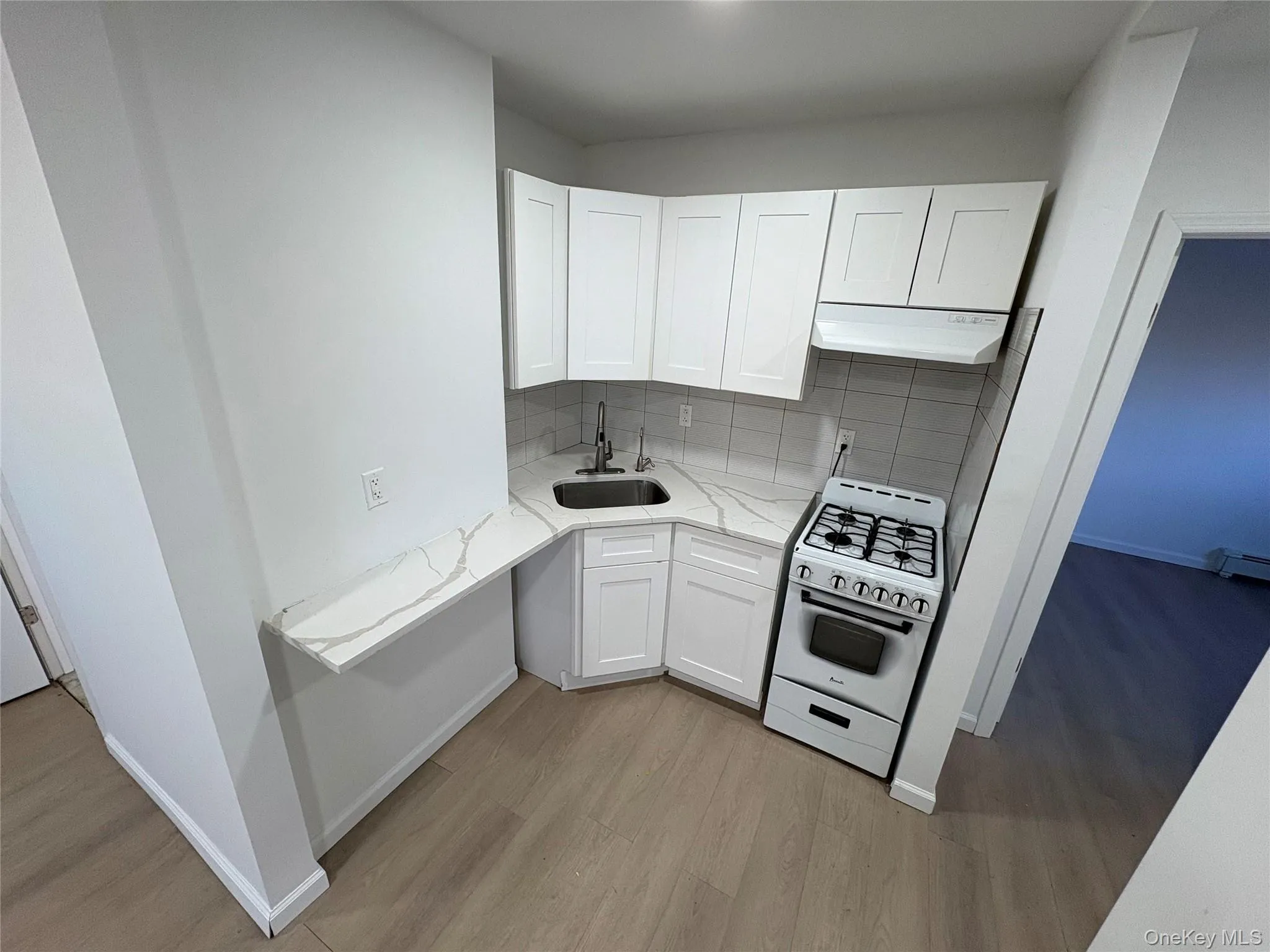 Kitchen with white gas range oven, white cabinetry, light stone countertops, decorative backsplash, and under cabinet range hood Kitchen with white gas range oven, white cabinetry, light stone countertops, decorative backsplash, and under cabinet range hood