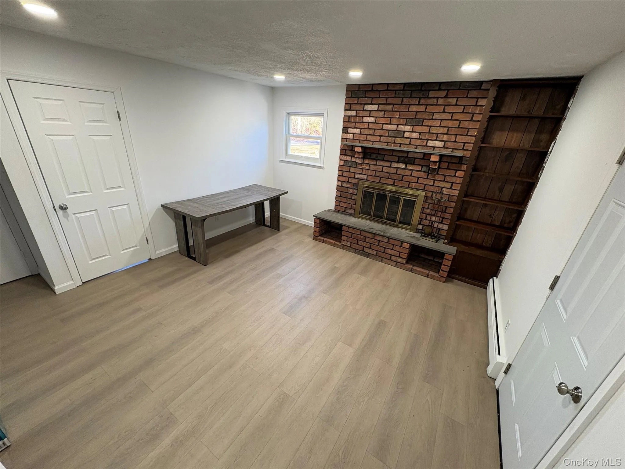 Unfurnished living room with a textured ceiling, a fireplace, light wood finished floors, recessed lighting, and a baseboard radiator Unfurnished living room with a textured ceiling, a fireplace, light wood finished floors, recessed lighting, and a baseboard radiator