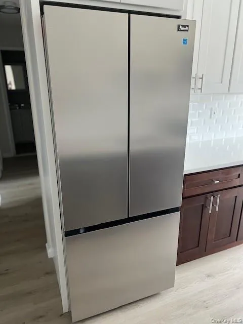 Kitchen view of freestanding refrigerator, light wood finished floors, dark brown cabinets, backsplash, and light stone counters Kitchen view of freestanding refrigerator, light wood finished floors, dark brown cabinets, backsplash, and light stone counters